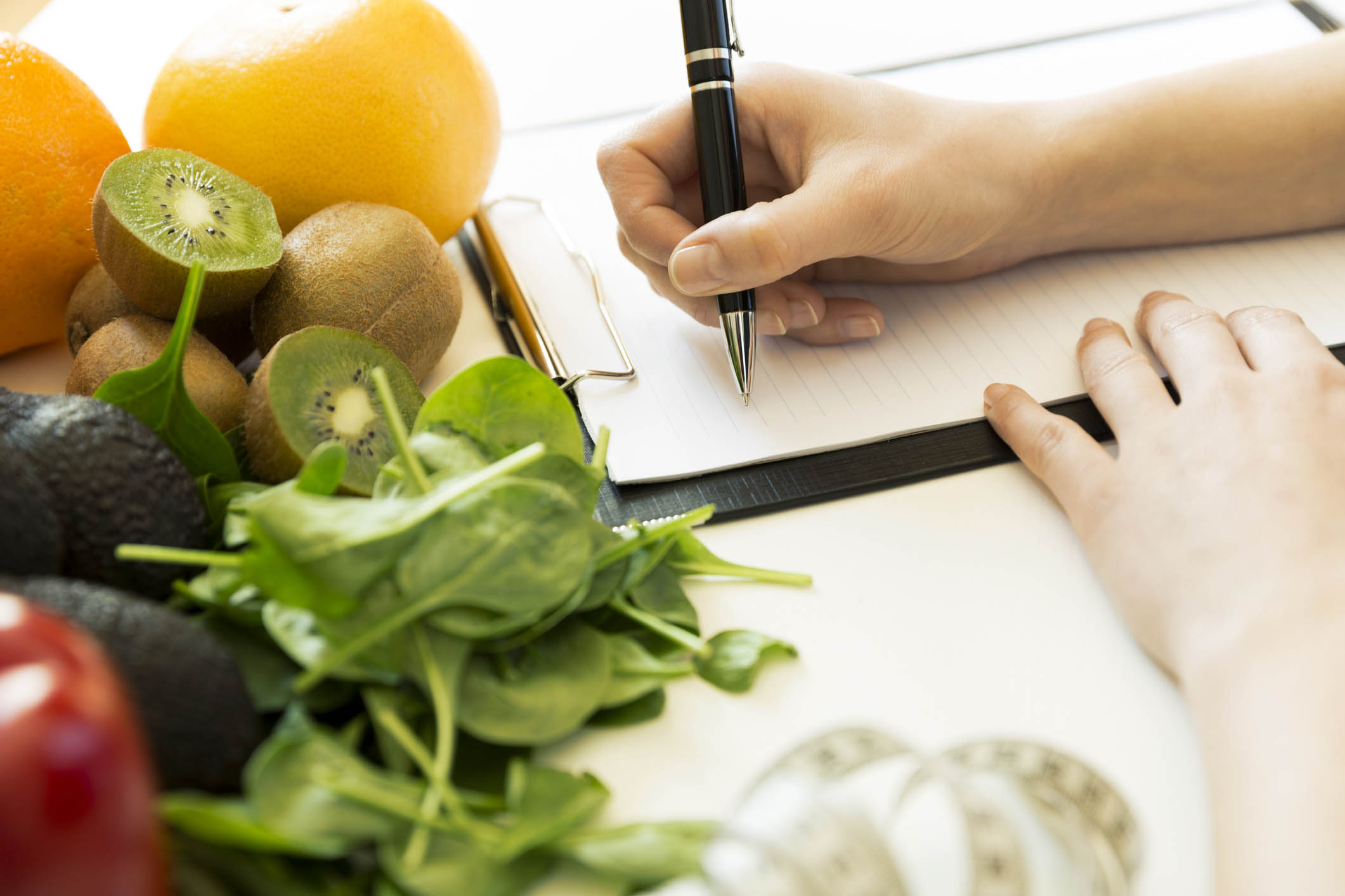 Nutritionist woman writing diet plan on table full of fruits and vegetables Nutritionist woman writing diet plan on table full of fruits and vegetables
